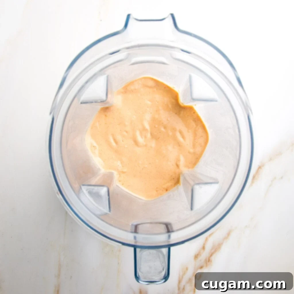 Creamy vegan chipotle dressing being poured from a blender into a glass jar.