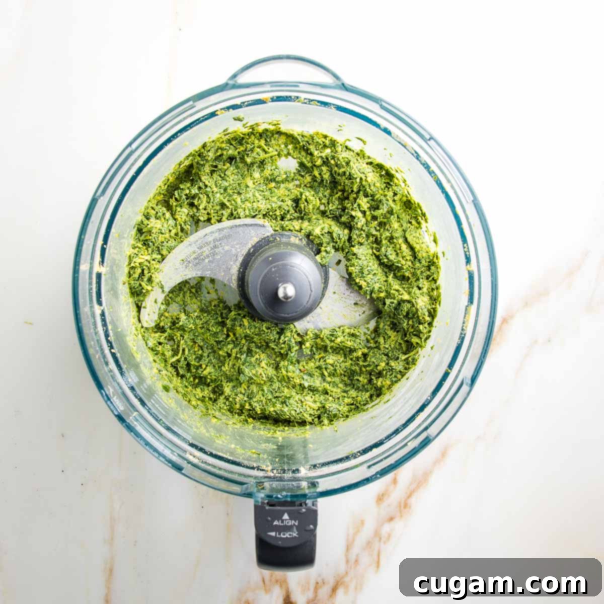 Pesto ingredients chopped into uniform pieces in a food processor bowl, appearing as a vibrant green, chunky mixture before the addition of liquid.