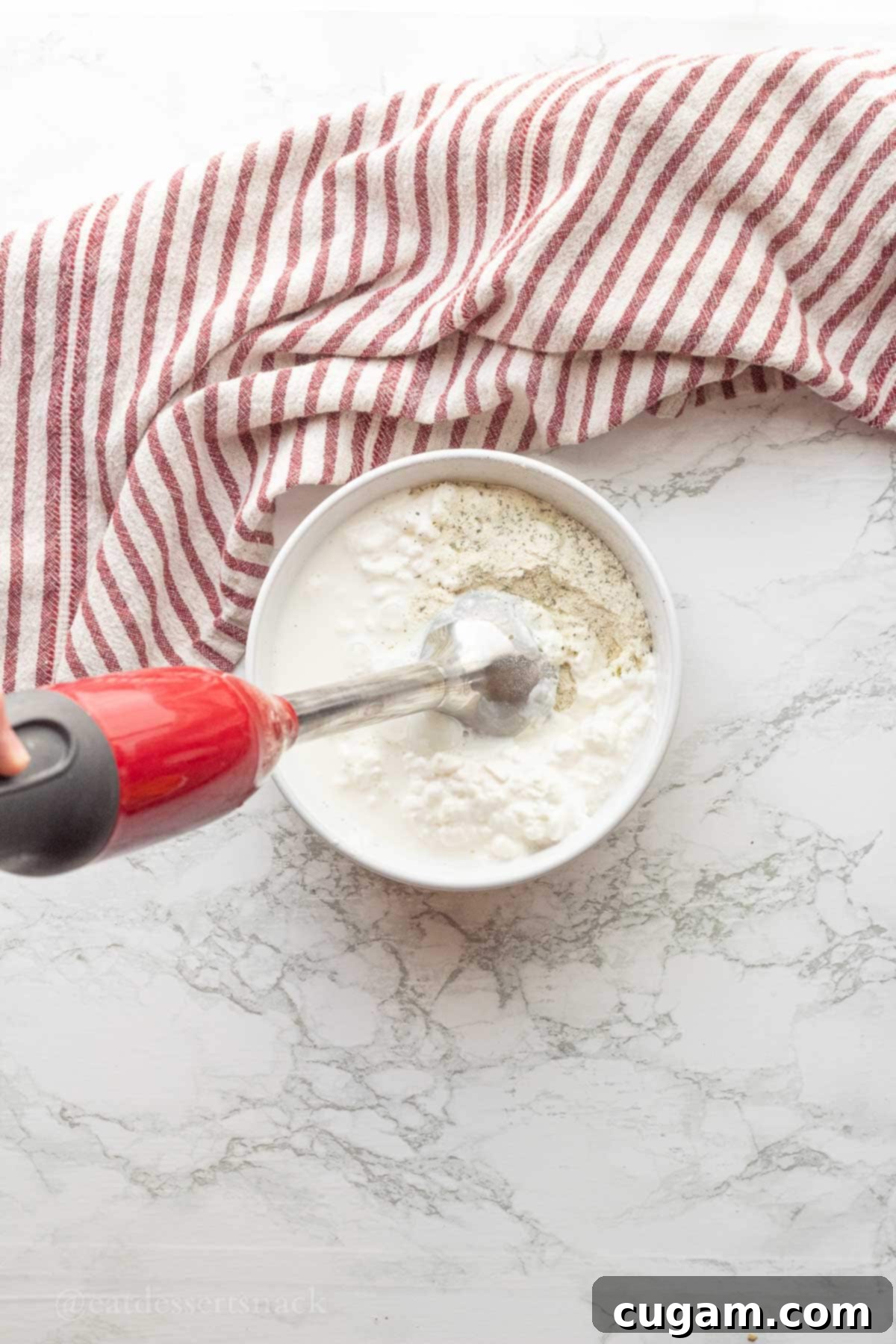 Blender submerged in a bowl of cottage cheese and ranch seasoning mix, beginning to blend.