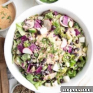White bowl filled with colorful chopped salad and an orange dressing, plus sunflower seeds. There is a small white bowl with same orange chipotle dressing on the side.