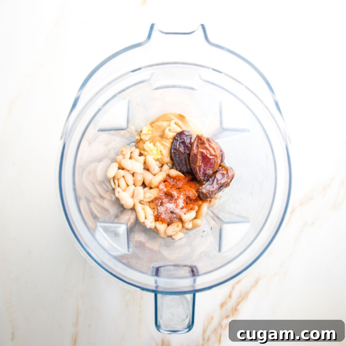 Blender pitcher filled with ingredients: white beans, dates, cashew butter, spices, garlic, vinegar.