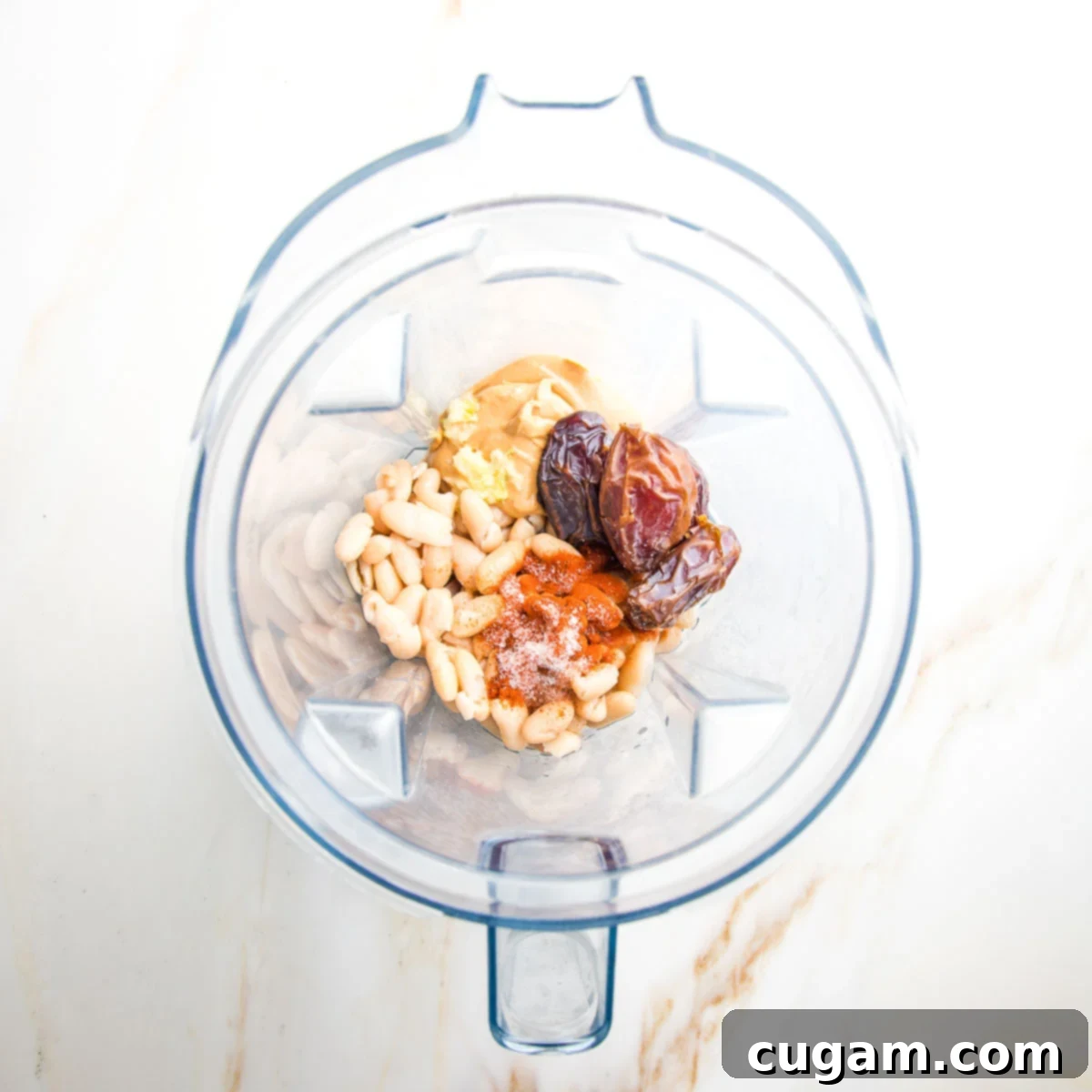 Blender pitcher filled with ingredients: white beans, dates, cashew butter, spices, garlic, vinegar.
