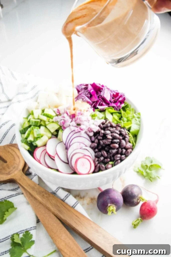 Prepared Mexican Chopped Salad in a large white bowl, partially dressed with chipotle dressing, with wooden salad tossers.