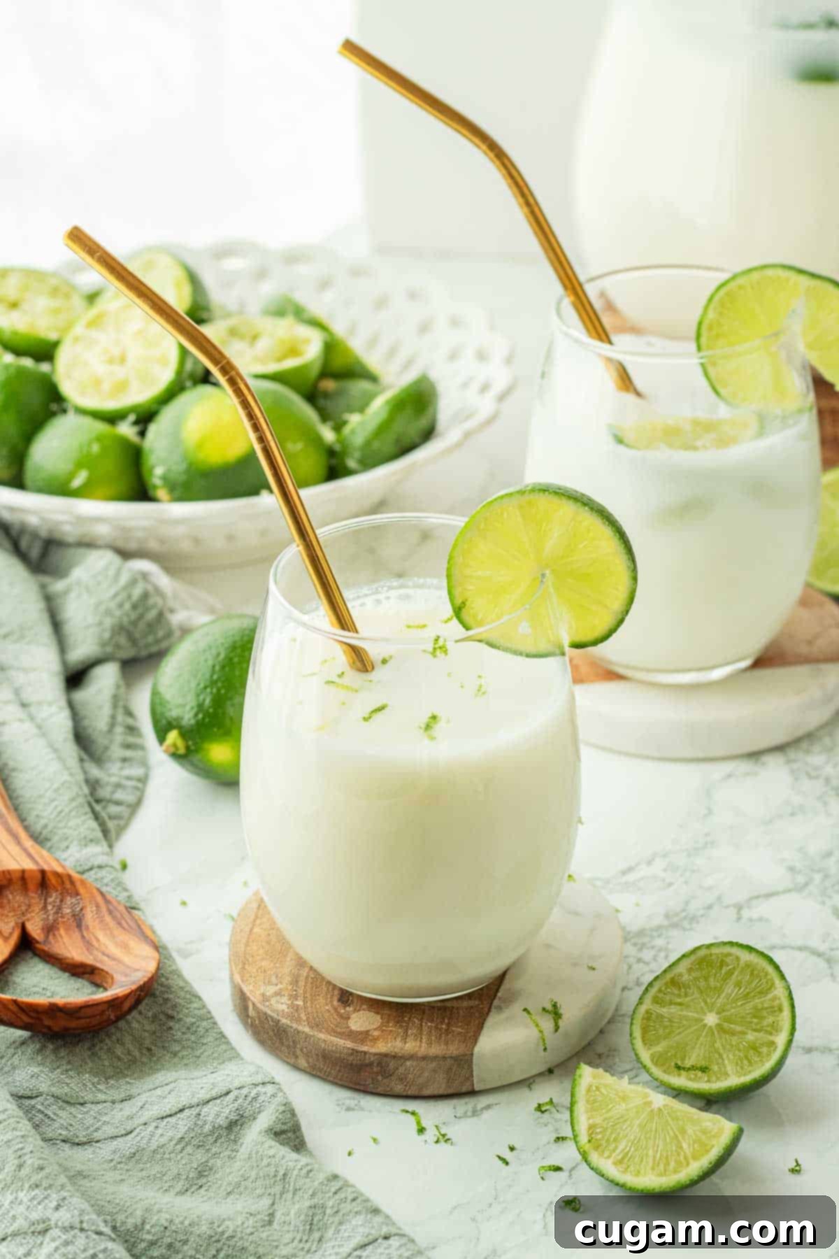 A glass of creamy Brazilian limeade with a gold straw and a fresh lime slice on the rim, resting on a marble coaster.