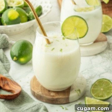 A beautifully presented glass of Brazilian limeade, complete with a gold straw and a fresh lime slice on the rim, sits on a stylish marble coaster.