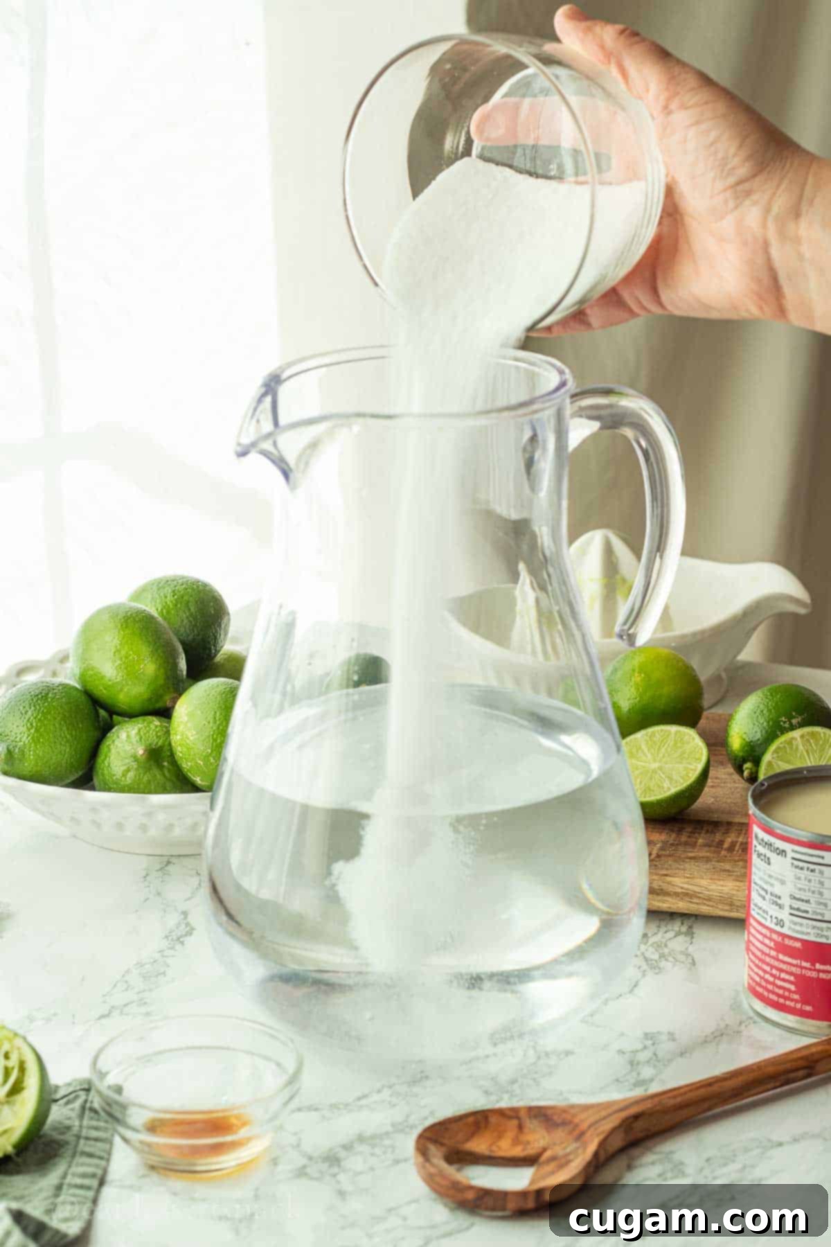 Pouring granulated sugar into a large pitcher filled with water.