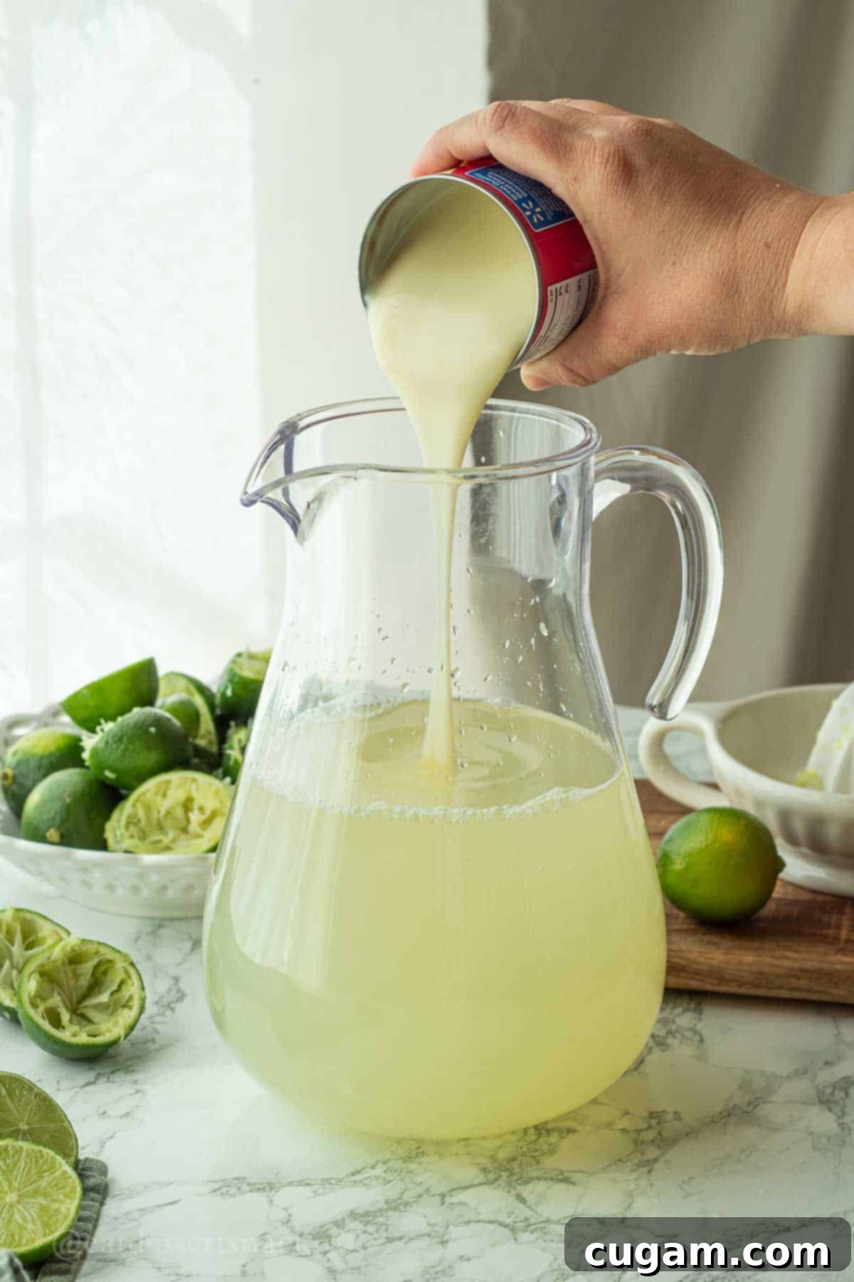 Pouring sweetened condensed milk into the pitcher containing the limeade mixture.
