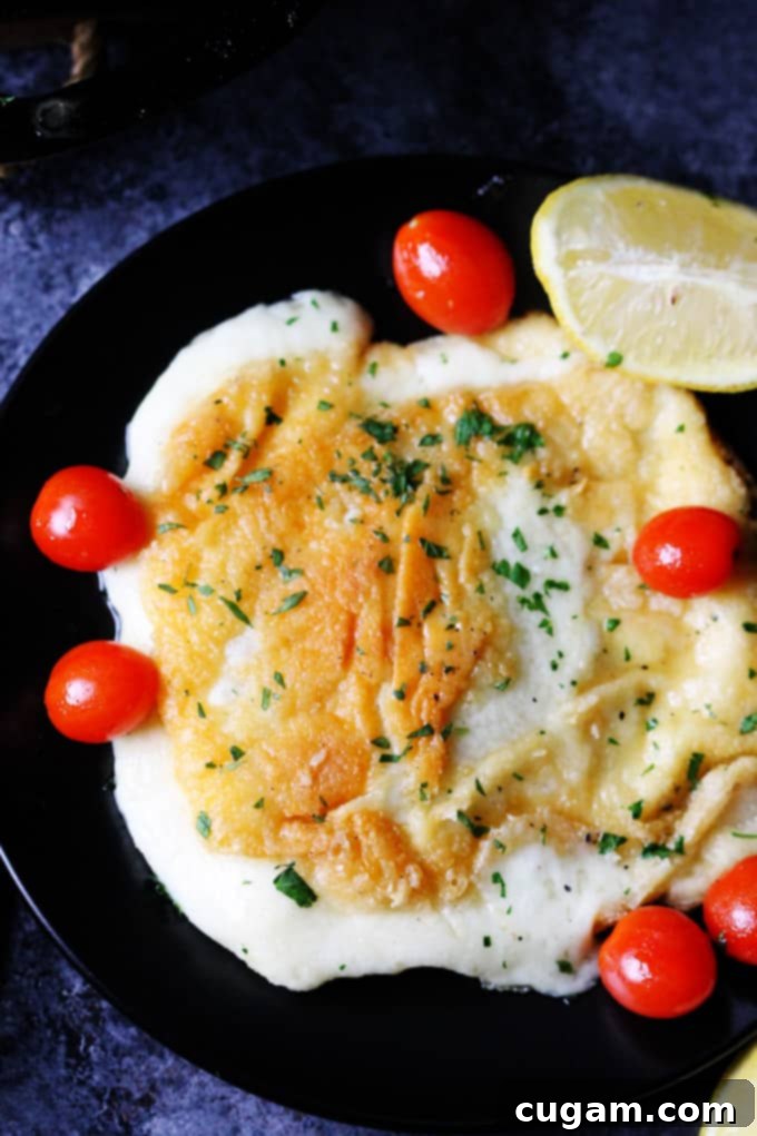 Golden-brown Greek Pan Fried Cheese Saganaki on a black plate with fresh tomatoes and lemon wedges