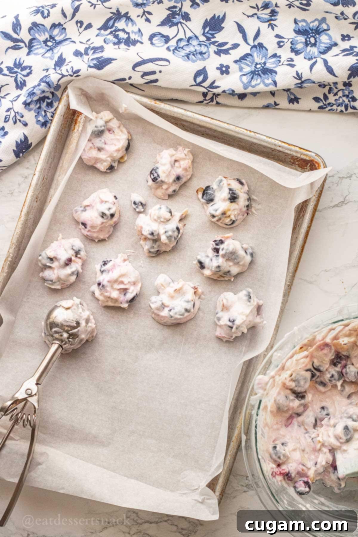 Frozen yogurt and blueberry clusters on cookie sheet with metal scoop.