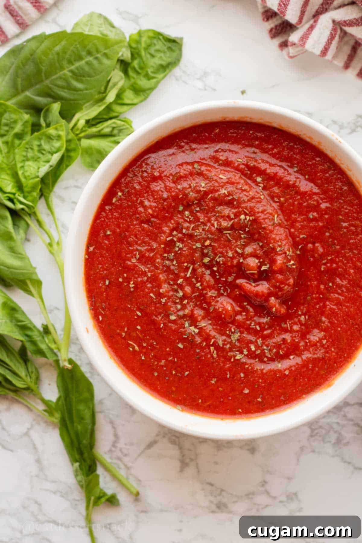 Thick homemade pizza sauce in a white bowl with fresh basil leaves, ready to be used on a pizza.