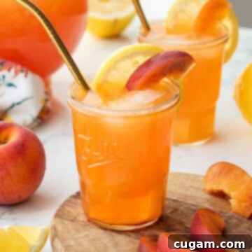 A glass of homemade brown sugar peach lemonade, garnished with fresh lemon and peach slices and a straw.