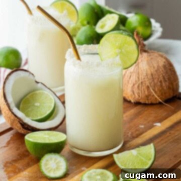 Glass of lime in the coconut drink with straw and lime slice and pitcher of limeade. With coconut shell nearby.