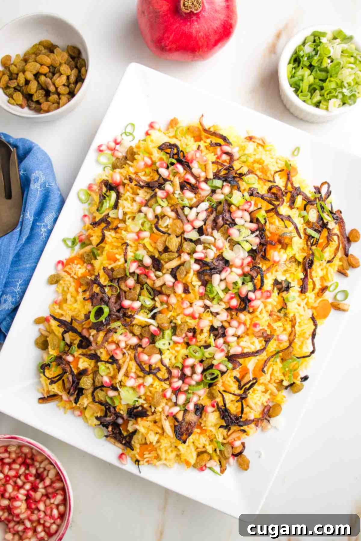 A vibrant platter of Jeweled Rice, adorned with ruby-red pomegranate arils, bright green pistachios, golden caramelized onions, and fresh scallions, promising a feast for the senses.