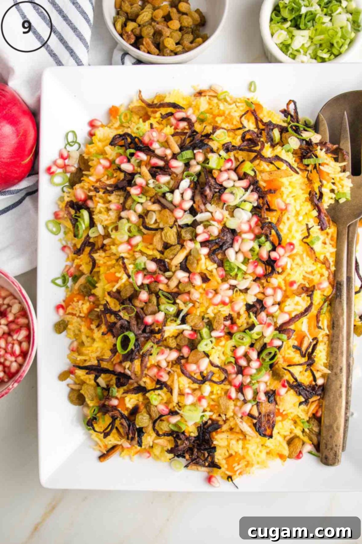 A grand platter showcasing beautifully layered Jeweled Rice, topped with a generous scattering of golden caramelized onions, fresh green scallions, ruby-red pomegranate seeds, and plump golden raisins, creating a vibrant feast for the eyes.