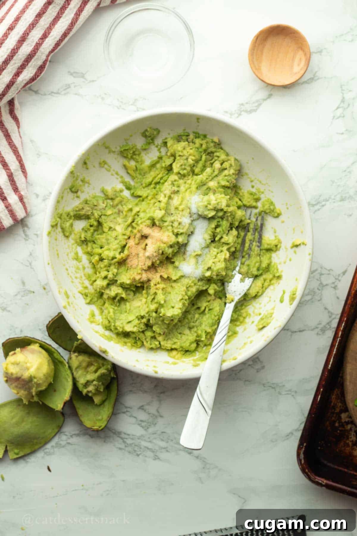 Mashing avocado with a fork in a bowl, with salt being added.