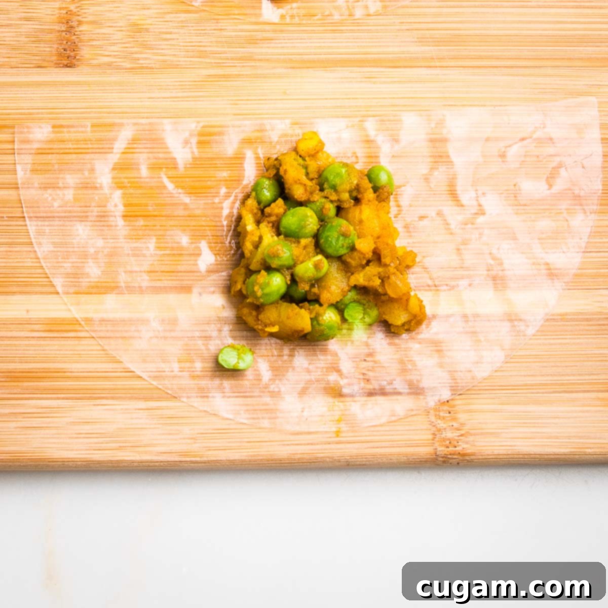 Half moon of moistened rice paper on a wooden board with a scoop of potato samosa filling