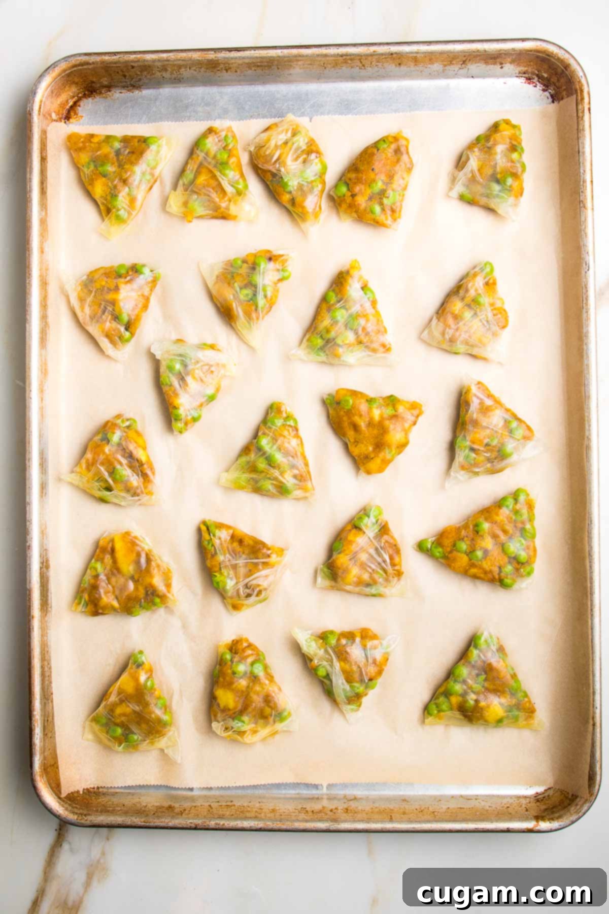 Triangle samosas in rice paper, filled with peas and potatoes, ready to bake.