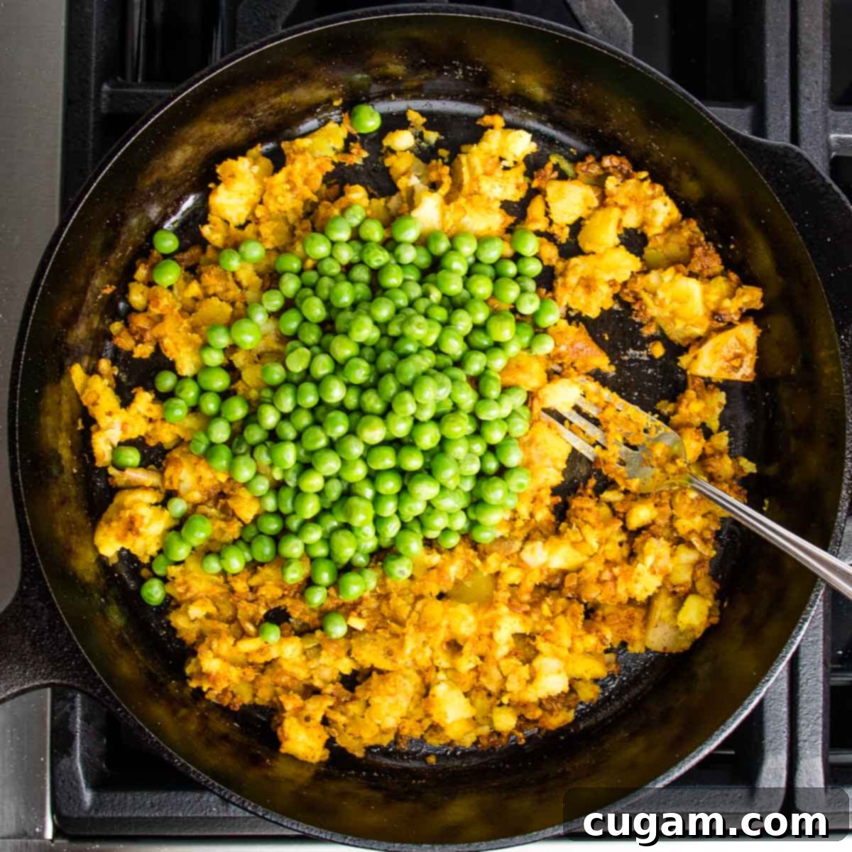 cast iron skillet filled with sauteed potatoes, onions and spices and a cup of peas on top