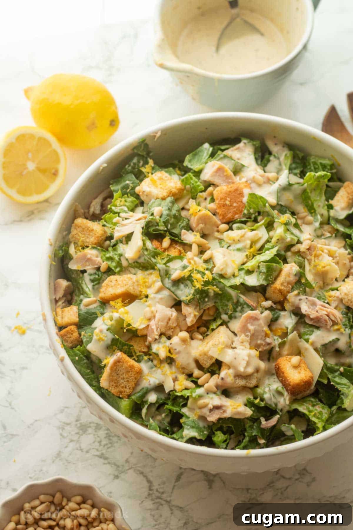 Lemon chicken caesar salad in bowl with lemons and croutons.