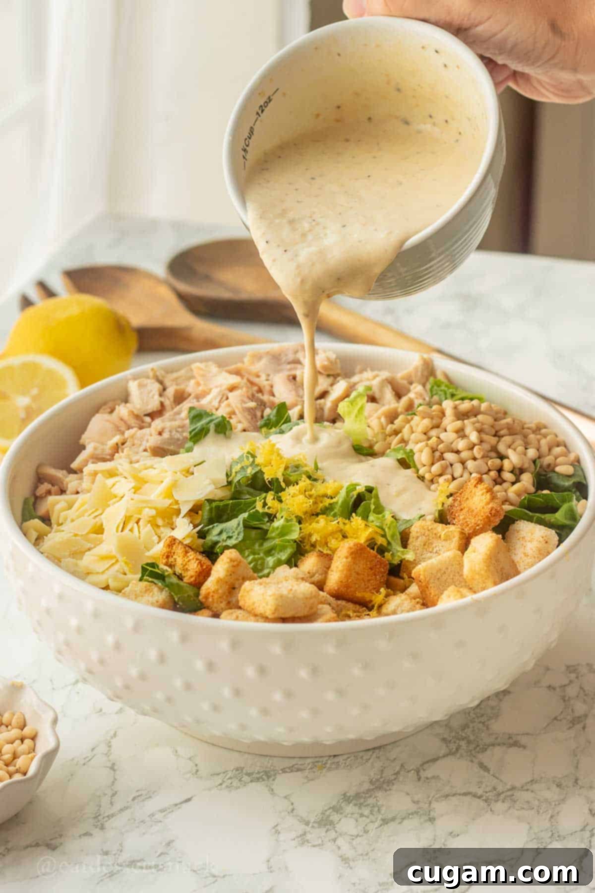 Pouring Caesar dressing onto salad in bowl.