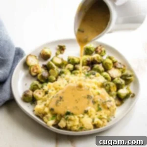 White pitcher pouring gravy over plate of chunky mashed potatoes and brussels sprouts