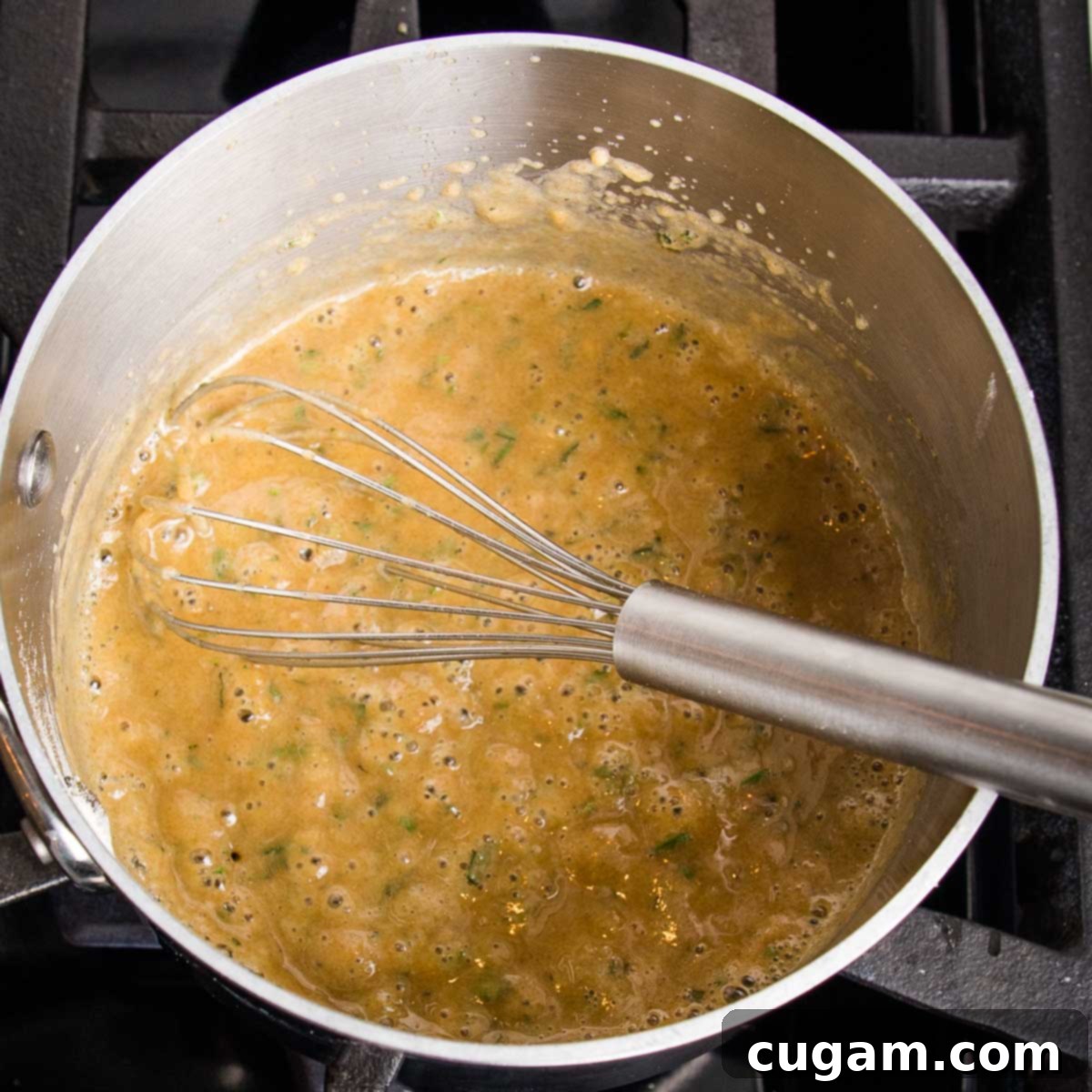 Small saucepan with a pasty mixture being whisked together. It's golden in color, speckled with flakes of fresh herbs.