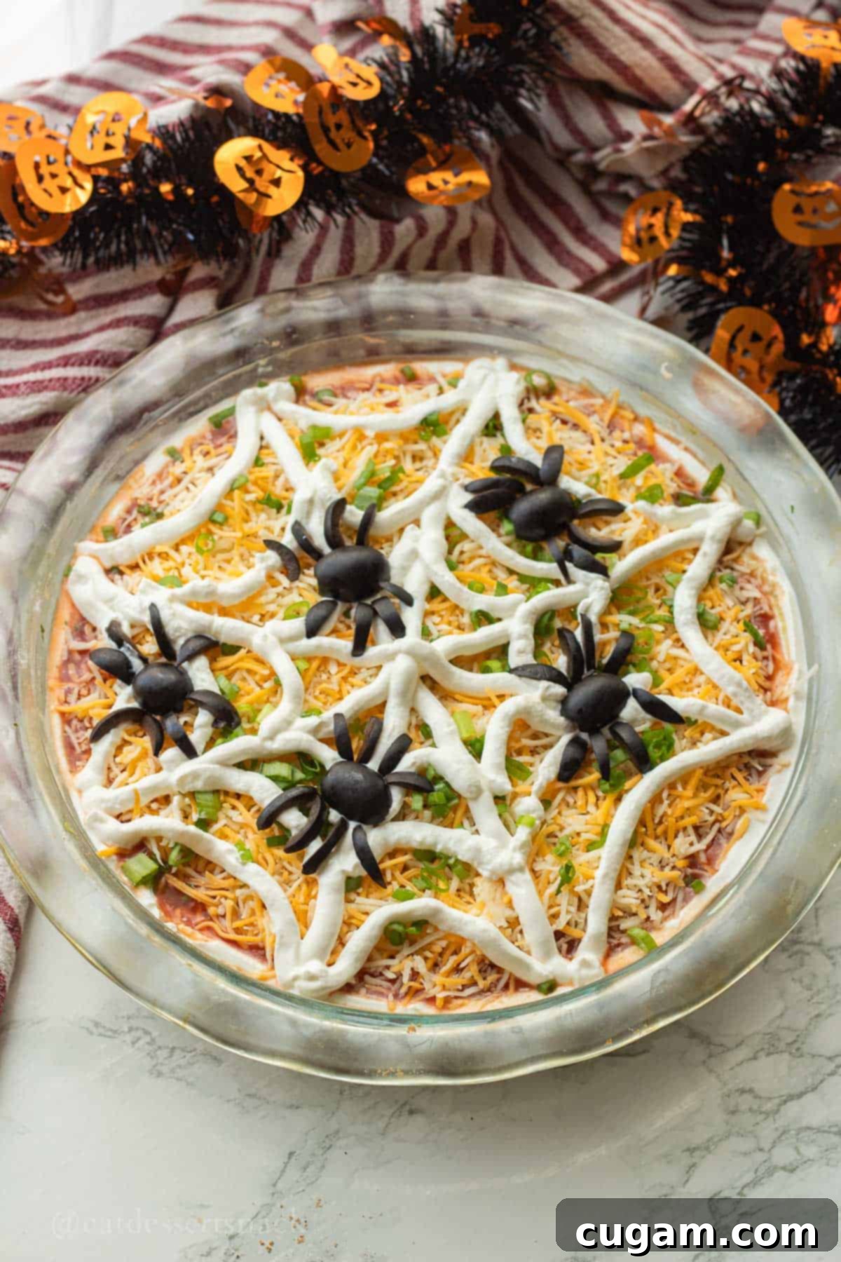 Spooky Spiderweb Taco Dip 2 Festive Halloween Spiderweb Taco Dip adorned with olive spiders on a sour cream web over a bean dip base.