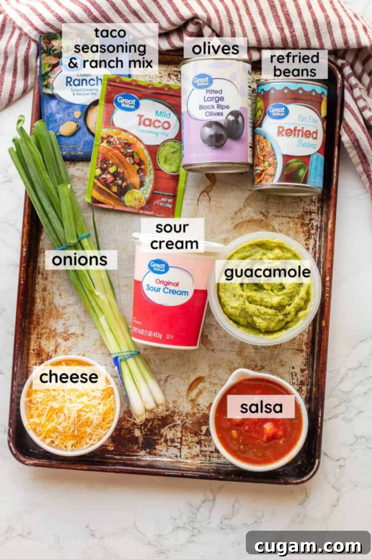 Spooky Spiderweb Taco Dip 3 A vibrant selection of ingredients for bean dip, including sour cream, fresh guacamole, tangy salsa, shredded cheese, and green onions, arranged in glass bowls on a metal baking pan.