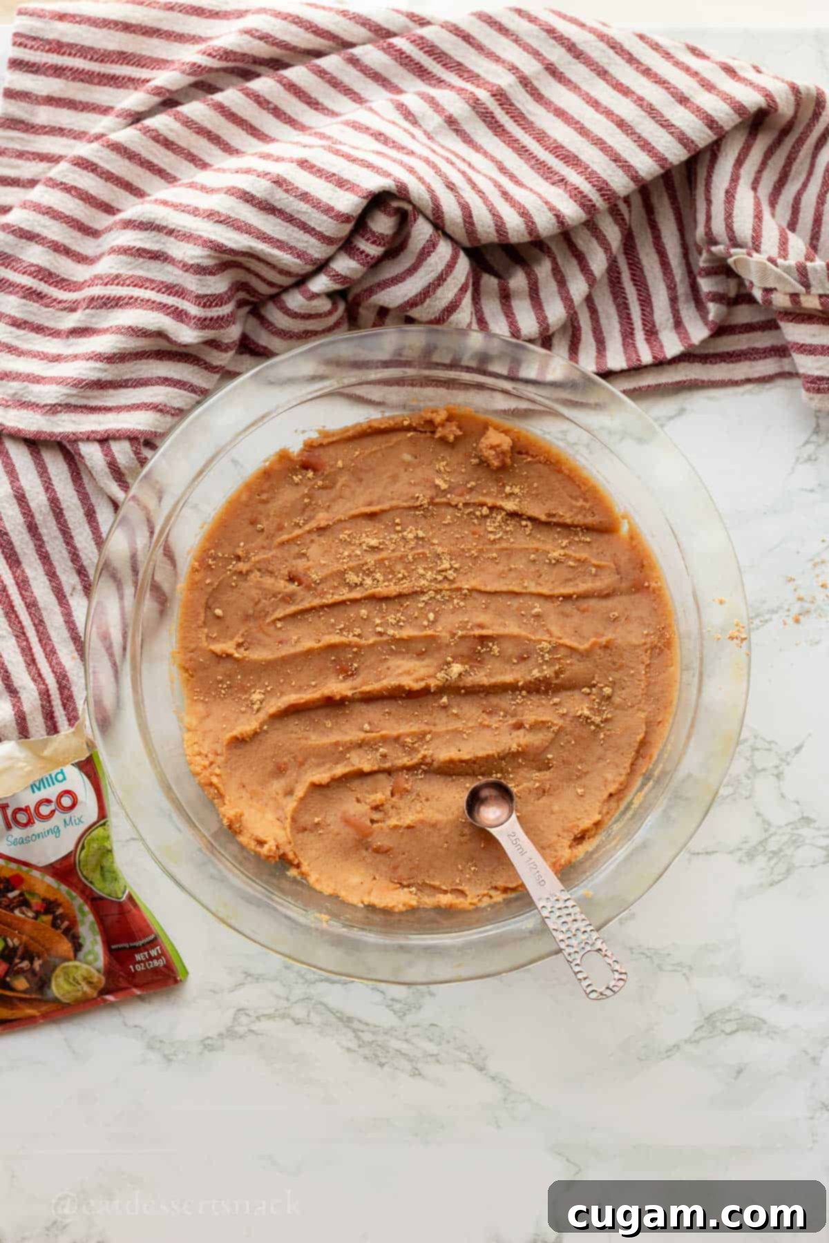 Spooky Spiderweb Taco Dip 4 Refried beans evenly spread in a pie pan, seasoned with taco seasoning for the base layer of the dip.