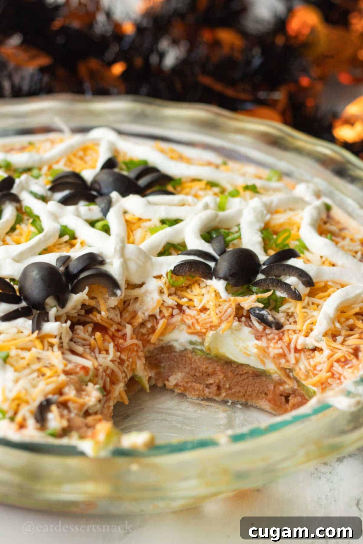 Spooky Spiderweb Taco Dip 10 A serving of the festive 5-layer bean dip with a spiderweb design carefully removed from the main dish, showcasing all the vibrant layers.