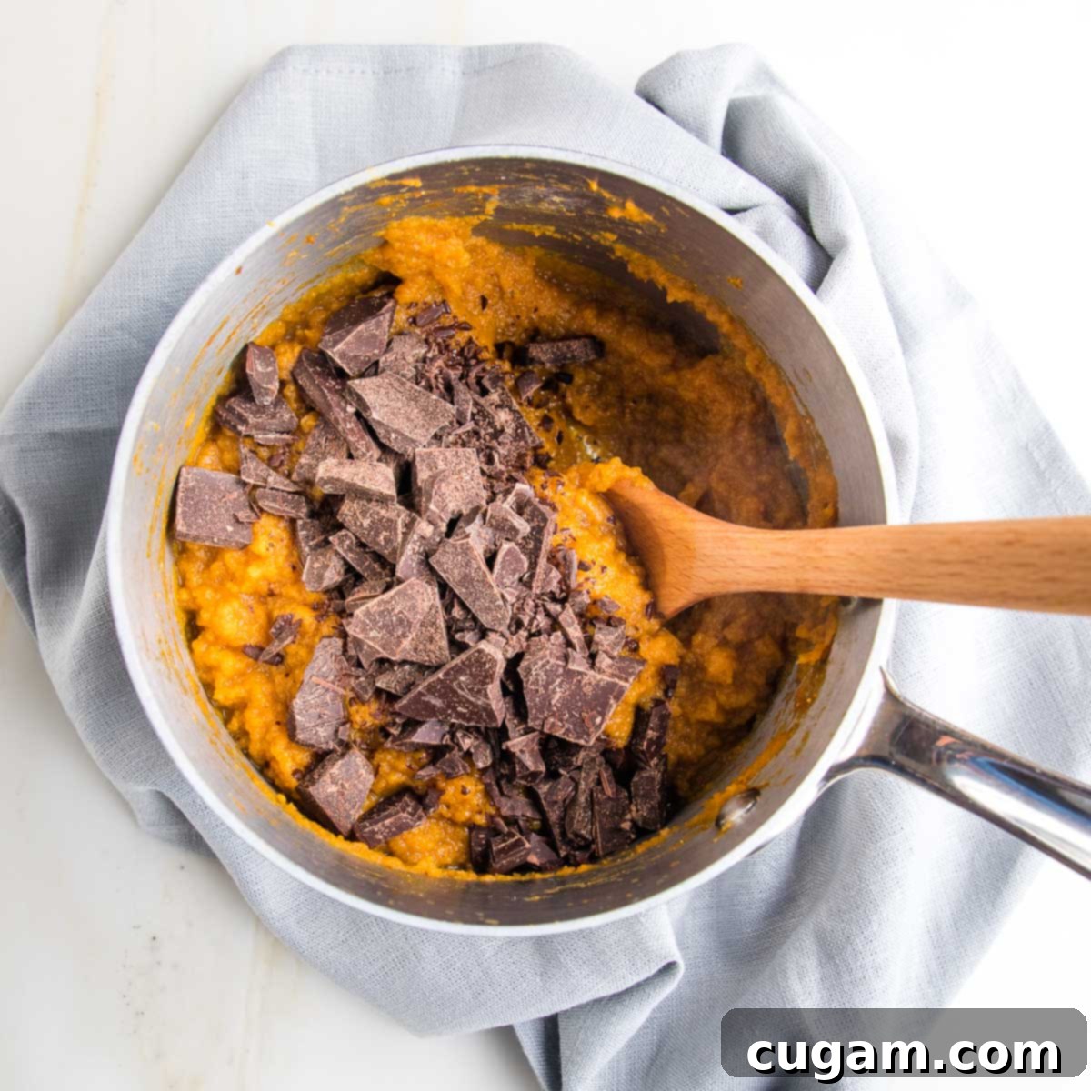 A small saucepan containing pumpkin puree and dark chocolate, being stirred gently with a wooden spoon as the chocolate melts into the pumpkin.