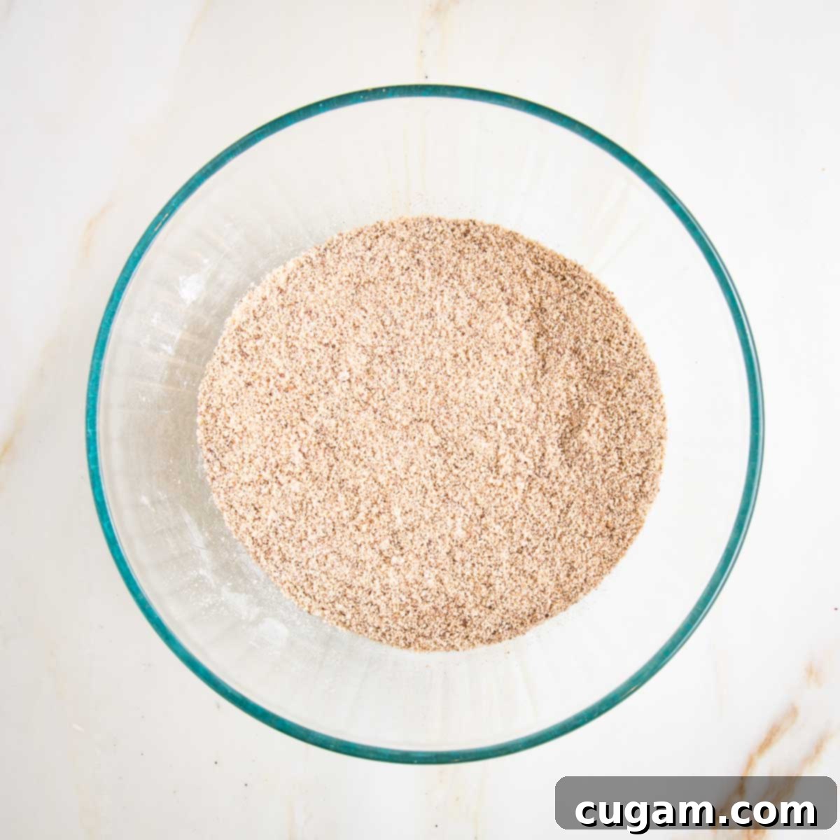 The dry ingredients for the pumpkin cake, mixed together into a uniform beige and brown blend in a glass bowl.