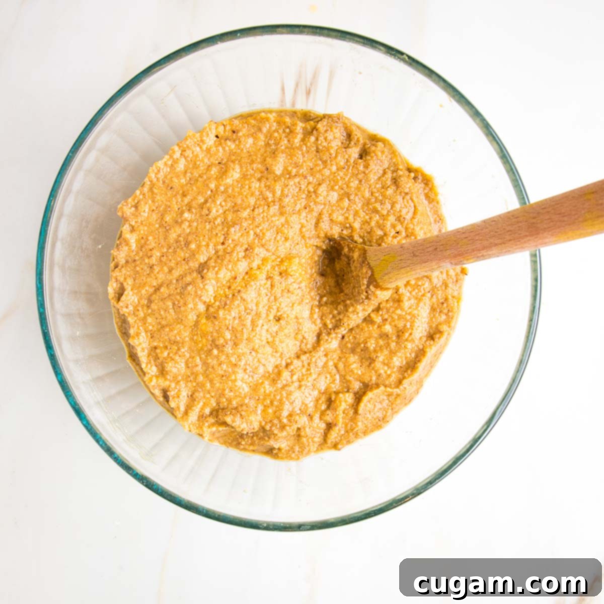 Pumpkin cake batter in a glass bowl, being gently mixed with a wooden spoon.