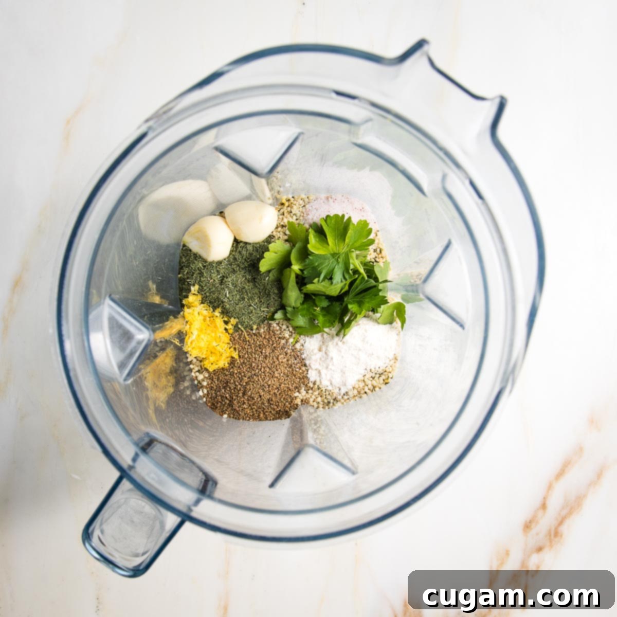 Healthy ranch dressing ingredients in a blender: you can see the lemon zest, parsley, garlic, celery seed, dill and hemp seeds, ready to be blended into a creamy dressing.