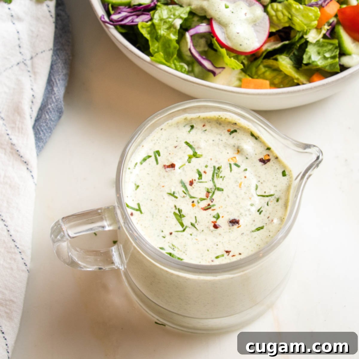 Close-up of a small glass pitcher filled with creamy vegan ranch dressing, showcasing its smooth texture and rich appearance.