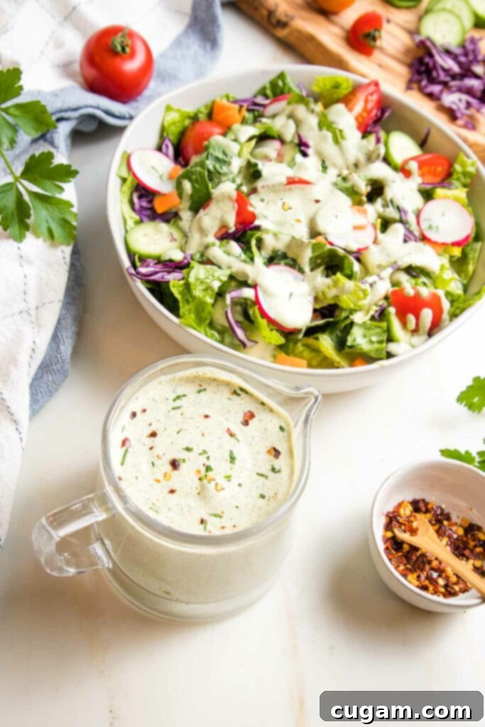 Vegan Ranch dressing in a glass pitcher, with some also seen drizzled generously over a simple green salad in the background, highlighting its versatile use.