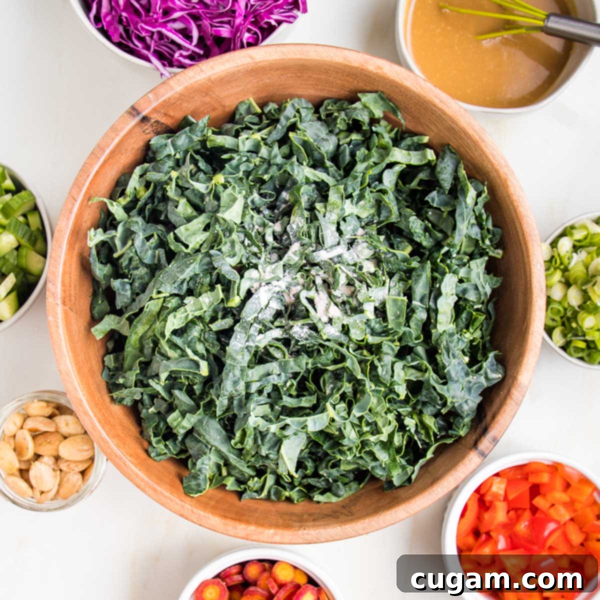Thinly sliced tuscan kale with small bowls of colorful ingredients all around the bowl of kale.
