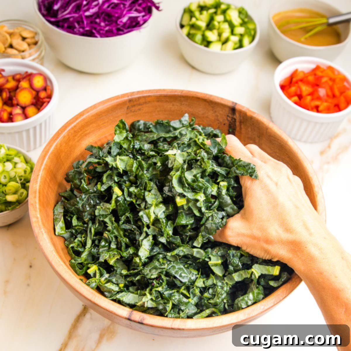 A hand gently massaging thinly sliced Tuscan kale in a wooden bowl with a sprinkle of sea salt, tenderizing the leaves.