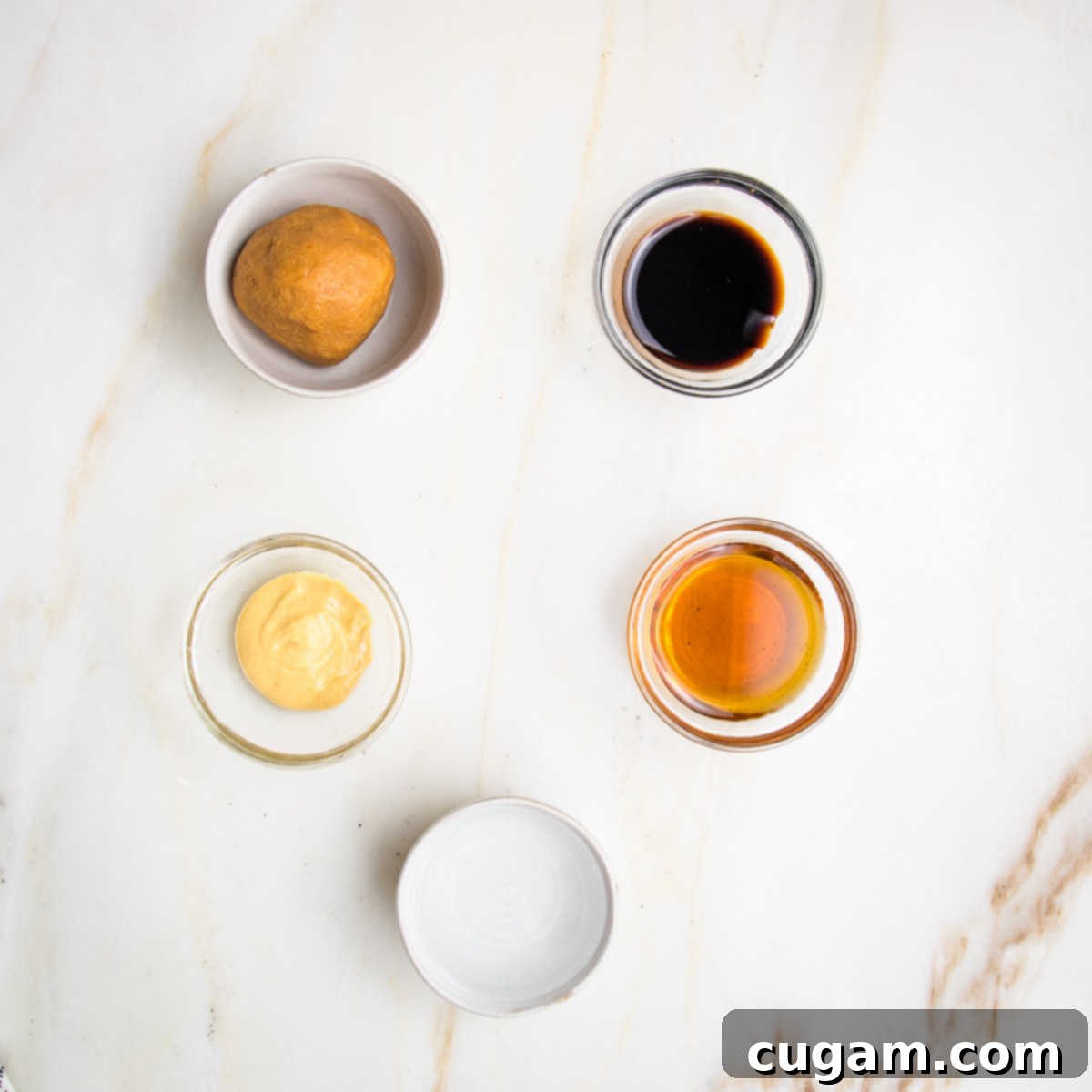 Small glass bowls containing the components of the miso dressing: light miso paste, balsamic vinegar, Dijon mustard, maple syrup, and water, arranged for mixing.