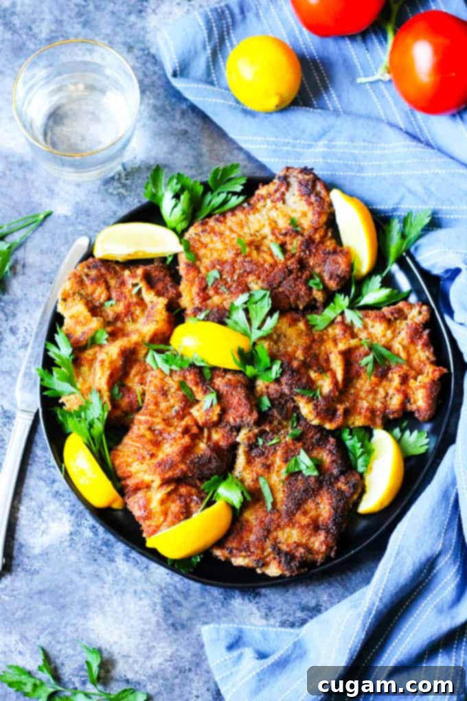 Veal cutlets Milanese style on a round black plate with blue background