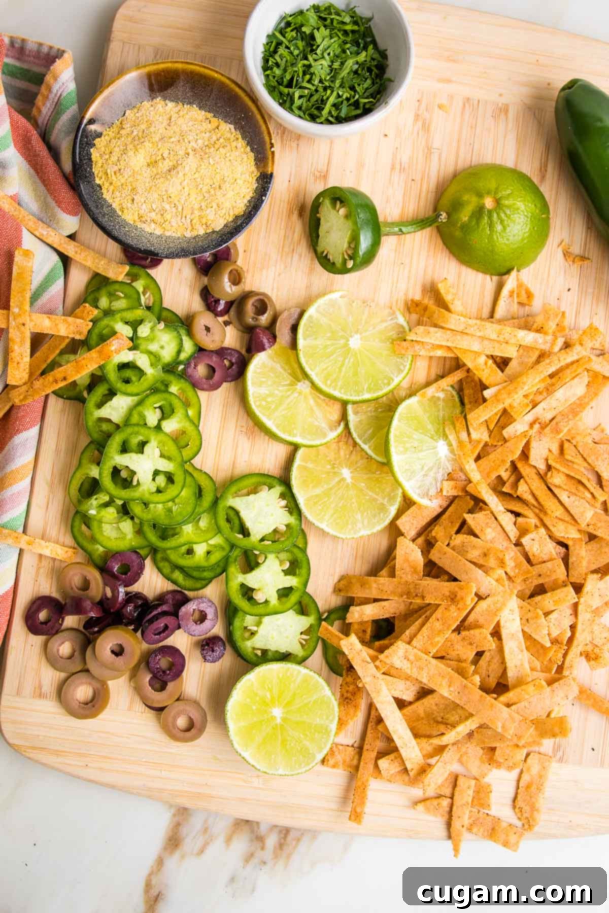 Cutting board with garnishes for vegan taco soup:  sliced jalapenos, nutritional yeast, lime wedges, chopped fresh jalapenos, baked tortilla strips. 