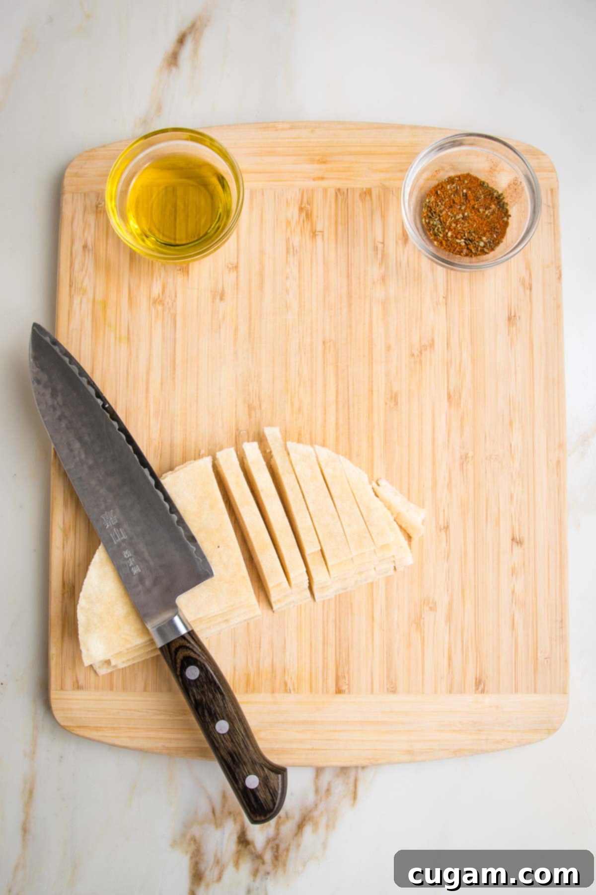 Almond flour tortillas stacked and being cut into strips on a wooden board. Also visible is a small dish of olive oil and another filled with taco seasonings.