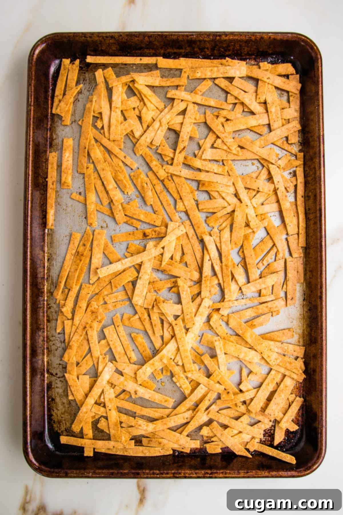Thin strips of baked almond flour tortillas on a rimmed baking tray with taco seasonings on them.