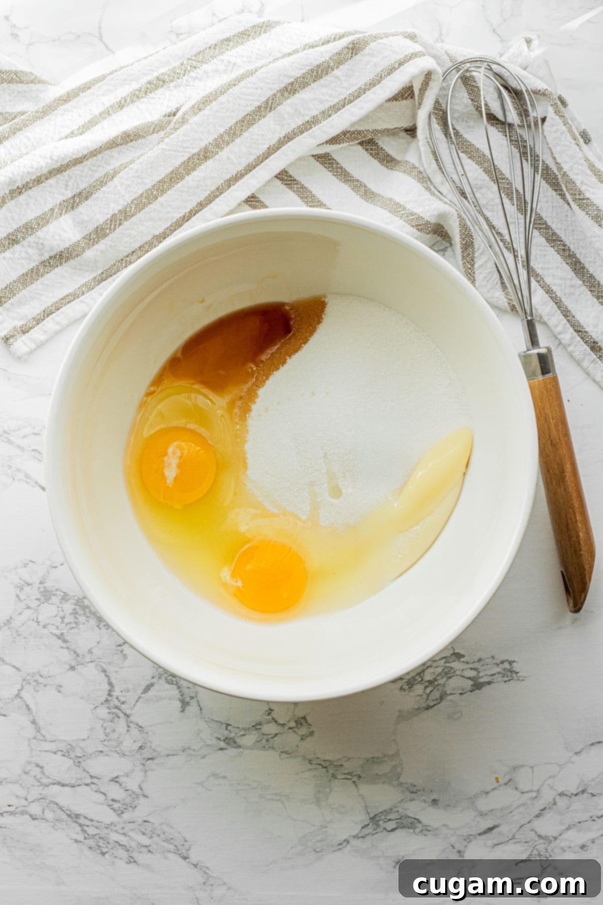 A large white mixing bowl containing white sugar, two whole eggs, sourdough discard, and vanilla extract, ready to be mixed into a fluffy batter.