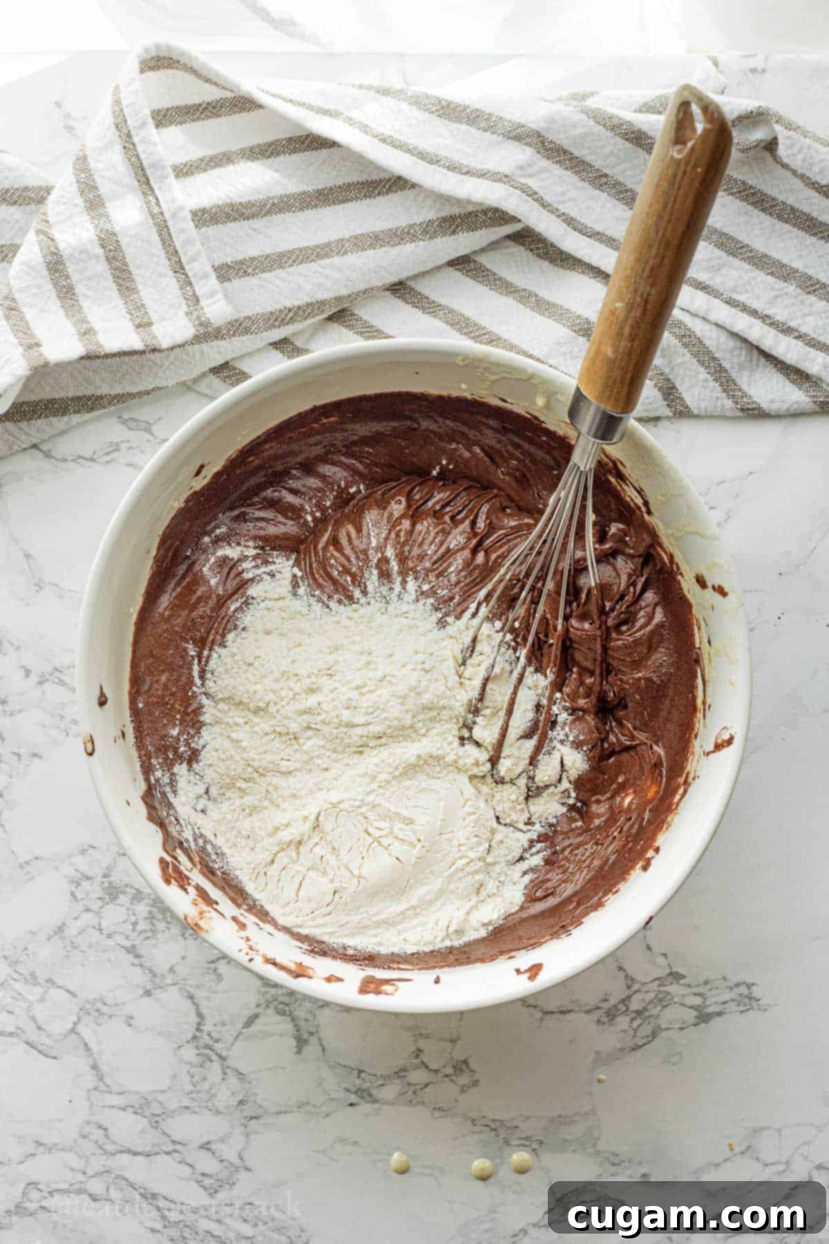 All-purpose flour and salt added on top of the dark, rich brownie batter in a white mixing bowl, ready for the final mixing stage.
