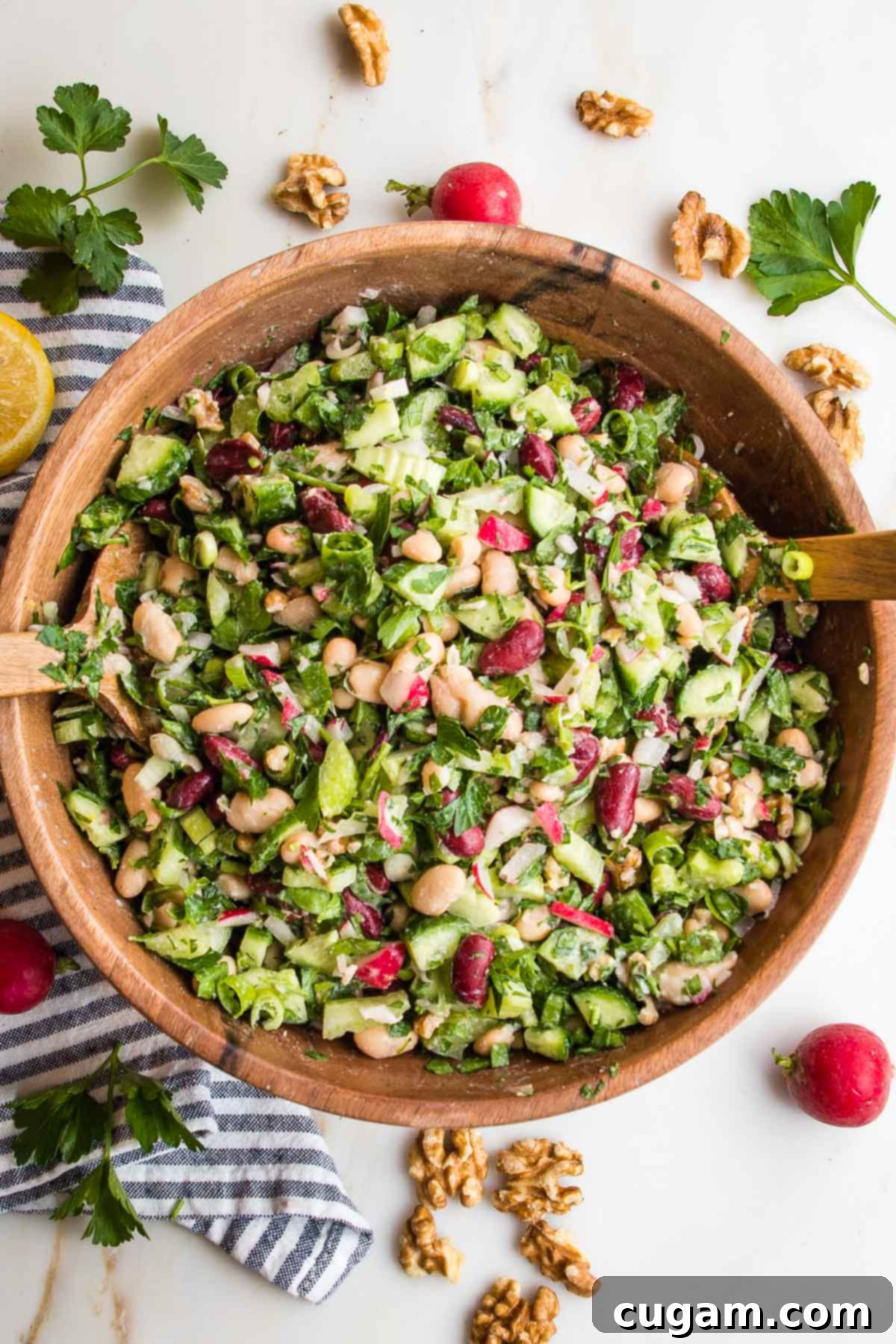Large wooden bowl filled with bean salad: chopped radish, white and red beans, chopped parsley, cucumbers, celery and scallions. 