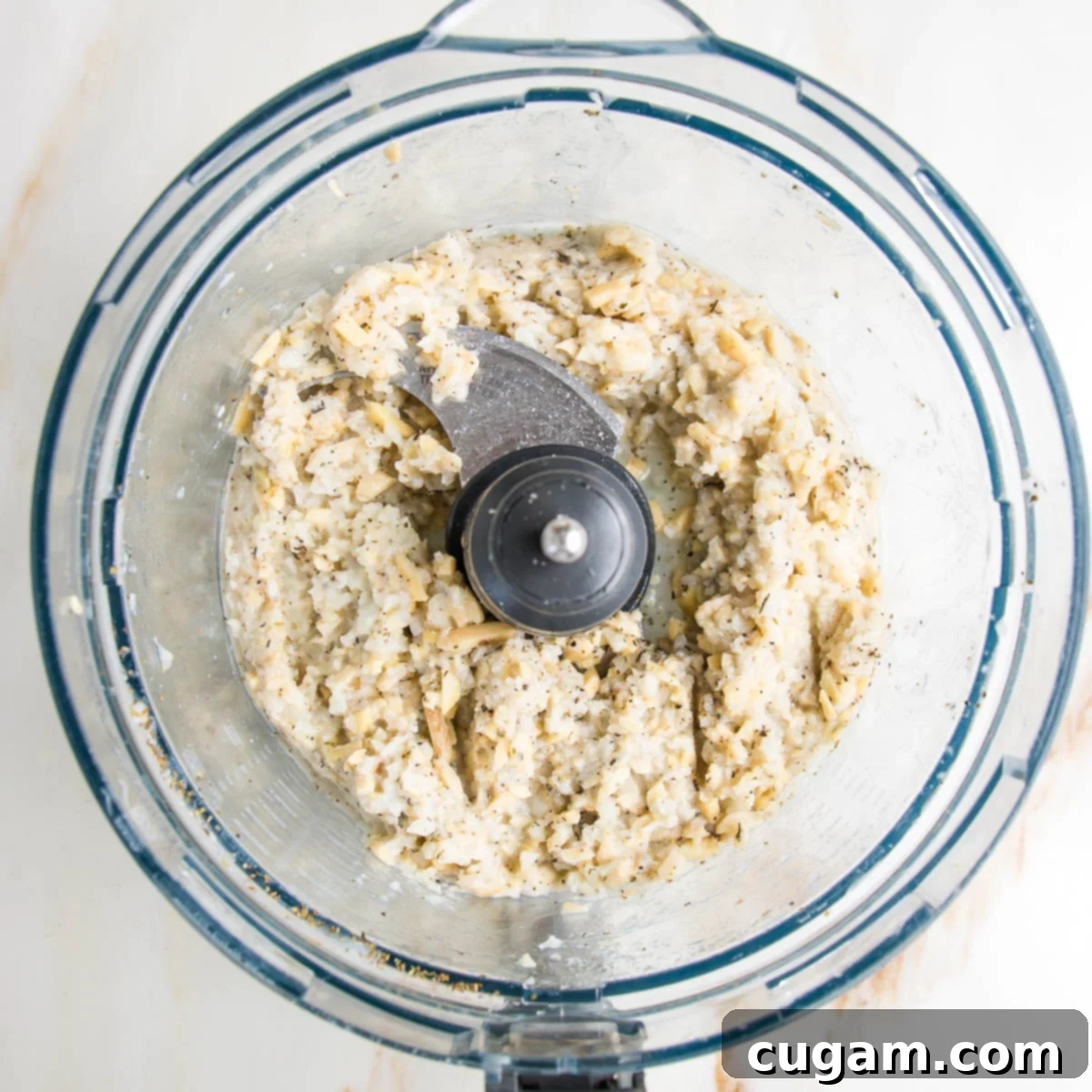 food processor bowl with chunks of partially blended cauliflower almond vegan ricotta.