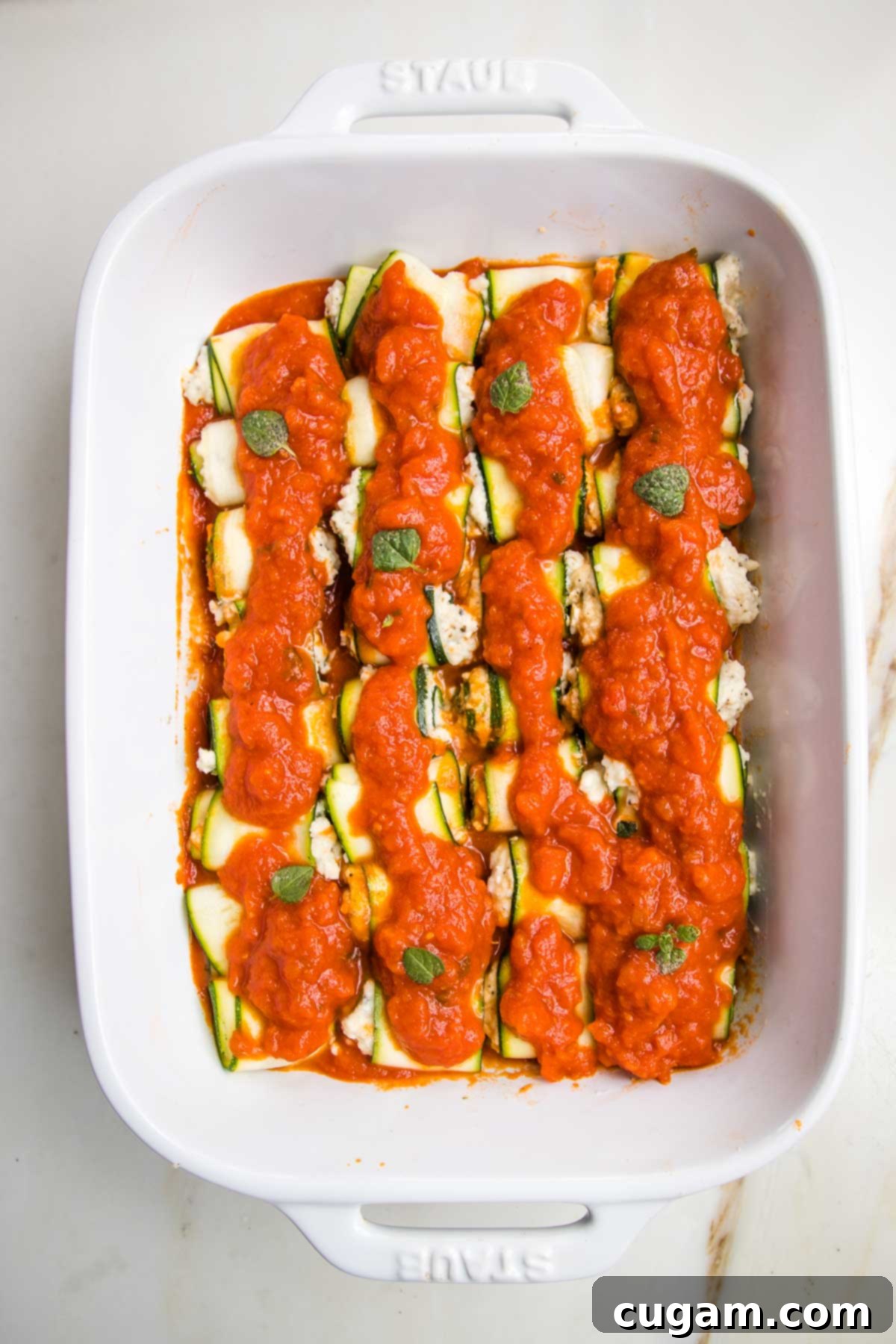 White baking pan with marinara, then zucchini ricotta roll ups and another layer of marinara