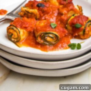Stack of white plates. On top is a plate full of zucchini roll ups filled with vegan ricotta and topped with marinara.