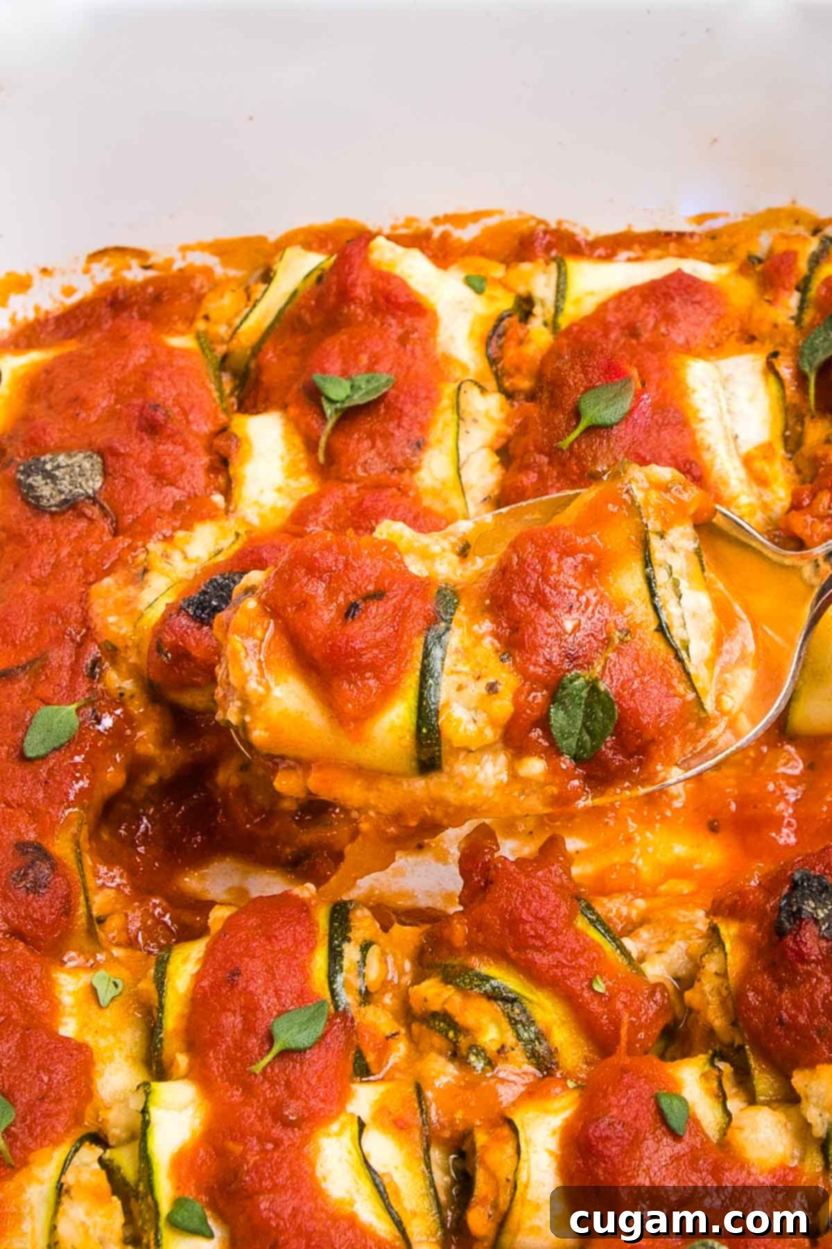 Zucchini stuffed with ricotta and baked in marinara sauce. A couple of the lasagna rolls are on a fork, shown close up.
